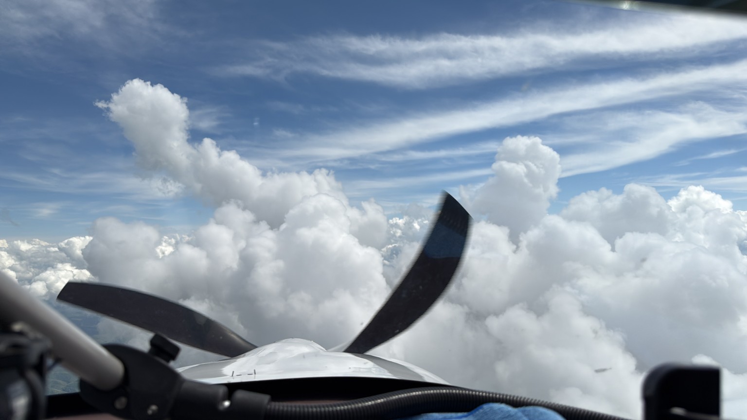 View over the nose and propeller of an airplane flying between towering clouds