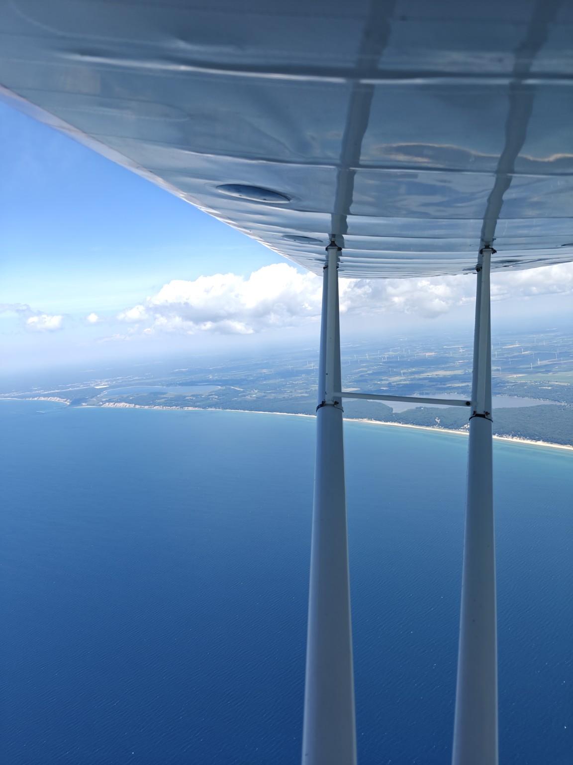 View past the wing struts of a small airplane over a blue lake and shoreline