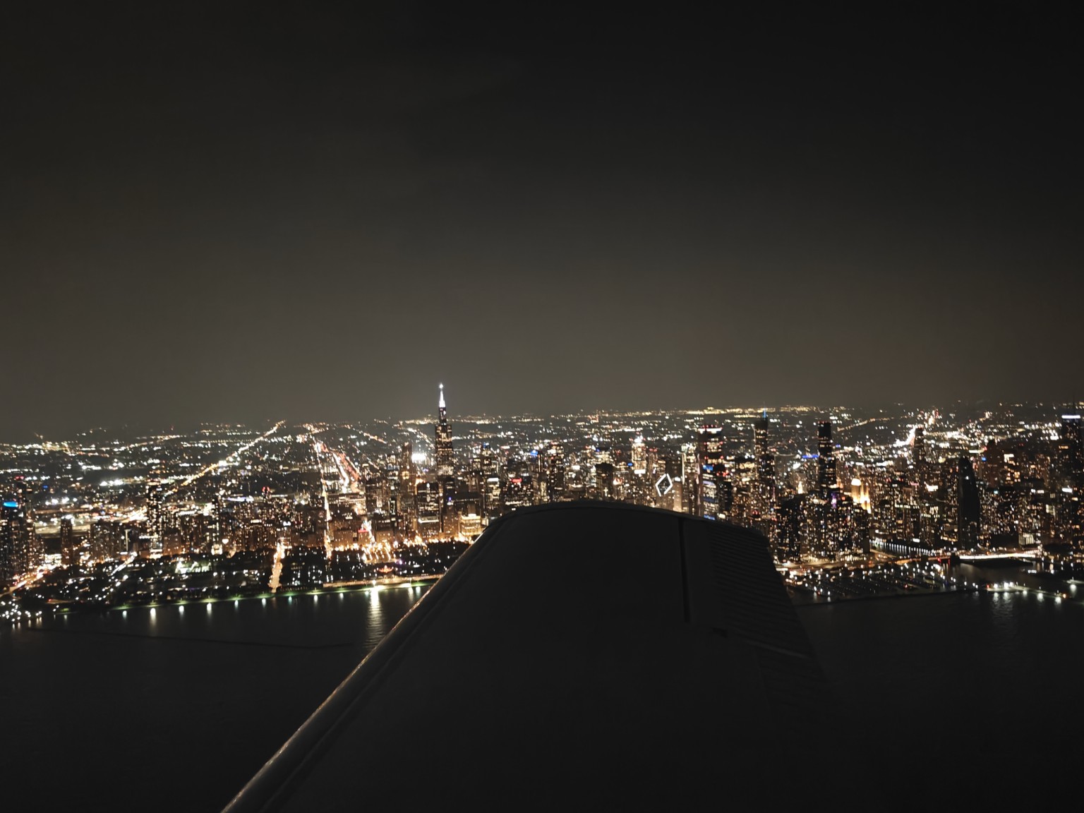 Night aerial view of a brightly lit city beyond an airplane wing